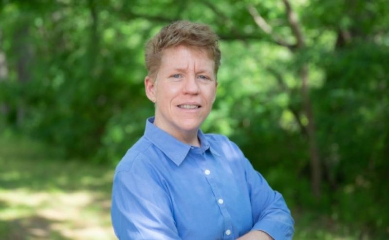 A bust-style headshot of Professor Kristen Renn in front of a background of green trees in the summertime.   